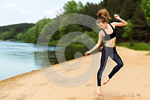 Young energetic girl who is engaged in fitness on the beach near the river