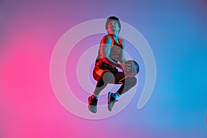 Young energetic man playing basketball  on gradient pink blue studio background in neon light. Youth, hobby