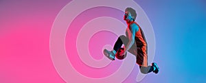 Young energetic man playing basketball isolated on gradient pink blue studio background in neon light. Youth, hobby