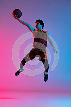 Young energetic man playing basketball isolated on gradient pink blue studio background in neon light. Youth, hobby