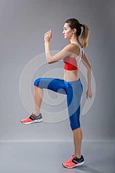 Young energetic woman walks highly lifting knees and waving the arms in the gym