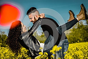 Young engaged couple kissing in a field of flowers man holding his girlfriend in his arms