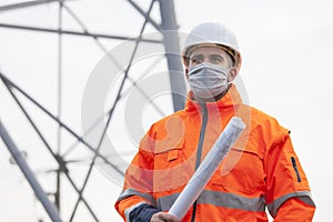 Young engineer or architect with face mask and plan in his hand on construction site