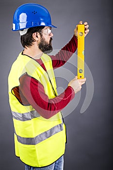 Young engineer with hardhat and reflective vest holding a leveler