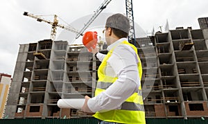 Young engineer holding blueprints and pointing at building site