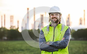 Young engineer standing outdoors by oil refinery, looking at camera.