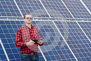 Young engineer with tablet computer standing near solar panels outdoors