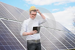 Young engineer with tablet computer standing near solar panels outdoors