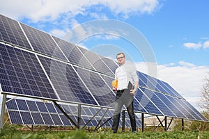 Young engineer with tablet computer standing near solar panels outdoors