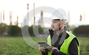 Young engineer with tablet standing outdoors by oil refinery. Copy space.