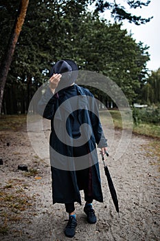 Young english man in stylish vintage coat and black hat walking in rainy forest