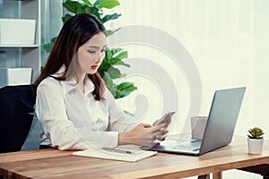 Young enthusiastic businesswoman using smartphone and laptop in office.