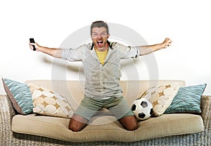 Young enthusiastic football fan celebrating goal crazy happy jumping on sofa couch at home watching soccer game on television hold