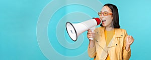 Young enthusiastic korean girl in trendy outfit, shouting in megaphone, making announcement, advertising, screaming in