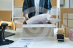 Young entrepreneur packing product in mailing box for shipping.