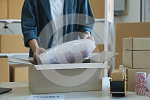 Young entrepreneur packing product in mailing box for shipping.