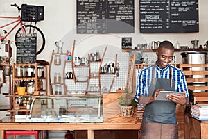 Young entrepreneur standing in his cafe using a digital tablet