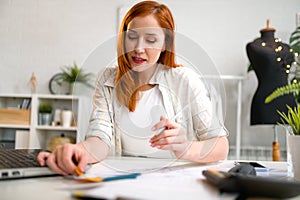 Young entrepreneur woman working in her small workshop, designing, calculating expenses, making business plan