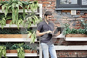 Young entrepreneur working outside using modern laptop. Standing near brick wall, plants, eco office. Successful business people