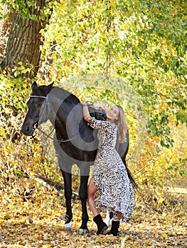 Young equestrian woman walking horse in autumn park