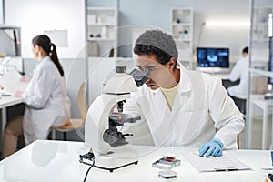Young ethnic man as scientist looking in microscope in laboratory