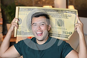 Young ethnic man holding gigantic 100 dollars bill