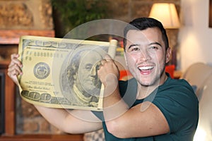 Young ethnic man holding gigantic 100 dollars bill