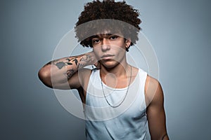 Young ethnic man with tattooed arm near gray background