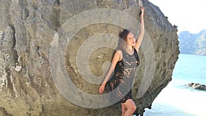 young european brunette girl poses by rock on sea coast