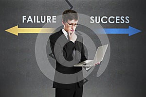 Young european businessman with laptop and failure and success arrows sketch on concrete background. Direction, growth, career