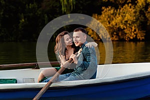 Young european couple is boating on a lake, young man and his girlfriend are sitting into boat at sunset, couple in love