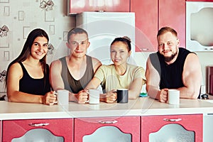 Young European couples in their 20s drinking hot drinks from mugs while sitting in front of kitchen island