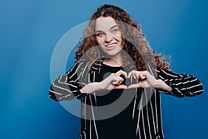 young European curly hair woman smiling and showing a heart shape with hands