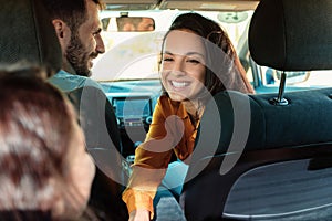 Young european family sitting in new car, mother smiling and talking to her daughter, enjoying road trip together