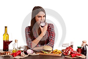 A girl, sits at a table with food and holds a half of onions and bites it. Isolated on white.