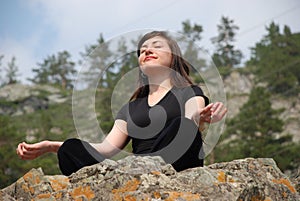 Young European girl meditates in mountains.