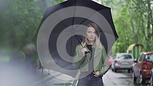 a young European girl stands with a black umbrella
