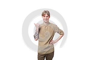 a young European guy with red hair is dressed in a fashionable beige shirt and brown trousers points his index finger to