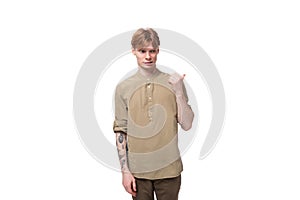 a young European guy with red hair is dressed in a fashionable beige shirt and brown trousers points his index finger to