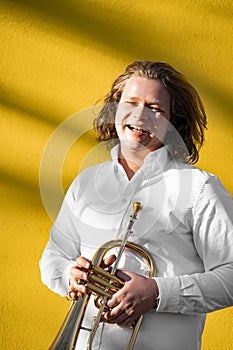 Young European male well-dressed cheerful smiling jazzman with trumpet outside