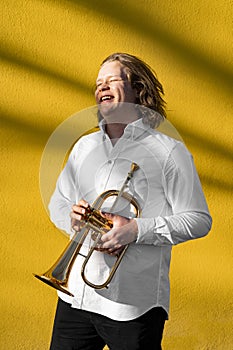 Young European male well-dressed cheerful smiling jazzman with trumpet outside
