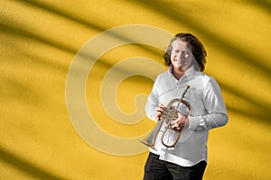 Young European male well-dressed cheerful smiling jazzman with trumpet outside