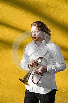 Young European male well-dressed serious posing jazzman with trumpet outside