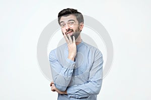 Young european man in blue shirt thinks, looks through incredulously