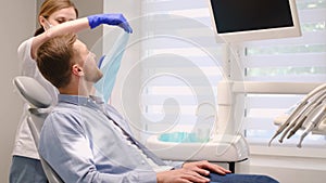 Young European man in a dental chair, he smiles at the doctor. Brushing teeth from caries