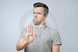Young european man in gray t-shirt showing with hand stop timeout gesture photo