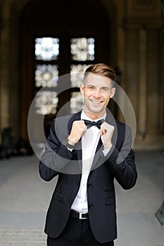 Young european man standing and posing, wearing black suit and bow tie.