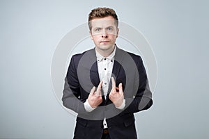 Young european man in suit pointing at himself, making excuses or verbally defending, having perplexed and puzzled look.