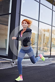 Young european redhead woman in sportive clothes running outdoors