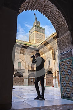 Young European tourist with a camera takes a picture in The Madrasa Bou Inania
